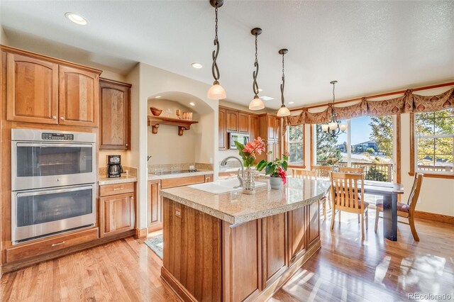 kitchen featuring decorative light fixtures, a kitchen island with sink, light hardwood / wood-style flooring, appliances with stainless steel finishes, and an inviting chandelier