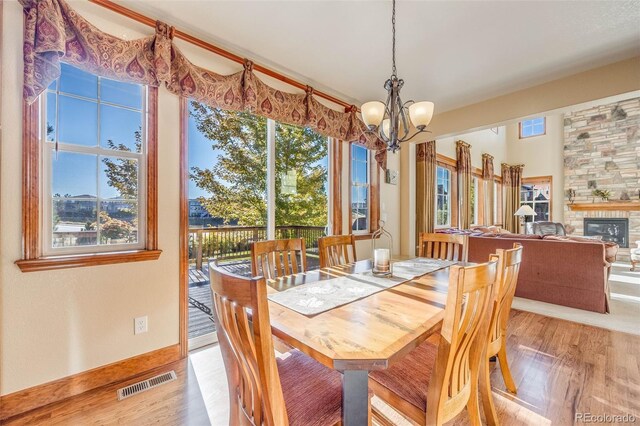 dining area with light wood-type flooring, a wealth of natural light, a stone fireplace, and a chandelier