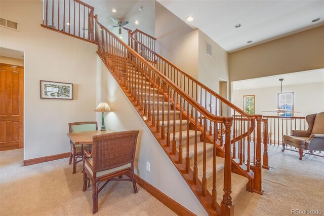 stairs featuring a high ceiling, ceiling fan, and carpet