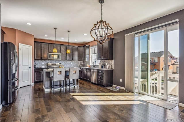 kitchen with appliances with stainless steel finishes, dark brown cabinets, a center island, dark hardwood / wood-style flooring, and decorative light fixtures