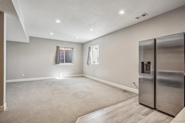 interior space featuring light carpet, stainless steel refrigerator with ice dispenser, and a textured ceiling