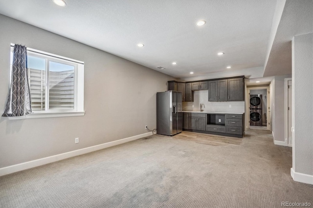 kitchen featuring light carpet, stainless steel fridge, dark brown cabinets, stacked washer / drying machine, and sink