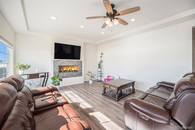 living area with light wood-style floors, a tray ceiling, a lit fireplace, and baseboards