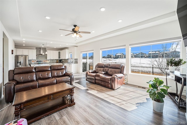 living room with light wood finished floors, baseboards, visible vents, a raised ceiling, and recessed lighting