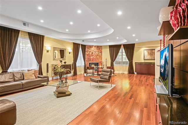 living room featuring light wood-type flooring, a tray ceiling, and a stone fireplace