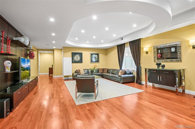 living room with light wood-type flooring and a raised ceiling