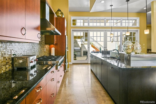 kitchen with hanging light fixtures, dark stone counters, wall chimney exhaust hood, and plenty of natural light