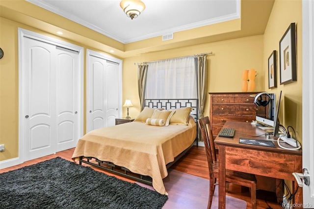 bedroom featuring a raised ceiling, ornamental molding, two closets, and dark wood-type flooring