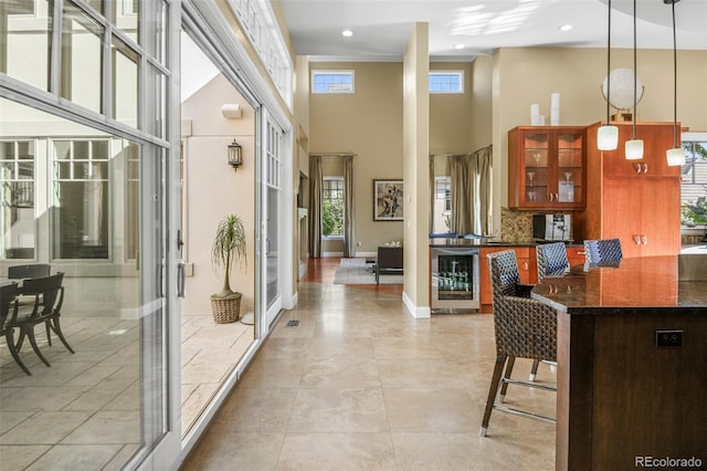 kitchen featuring beverage cooler, glass insert cabinets, a breakfast bar, a high ceiling, and backsplash