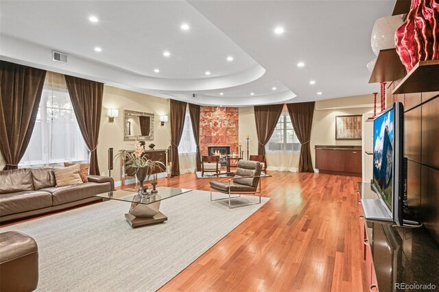 living area with recessed lighting, a fireplace, visible vents, light wood-type flooring, and a tray ceiling