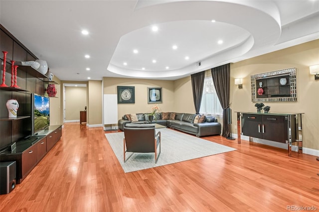 living area with a tray ceiling, light wood-style flooring, baseboards, and recessed lighting