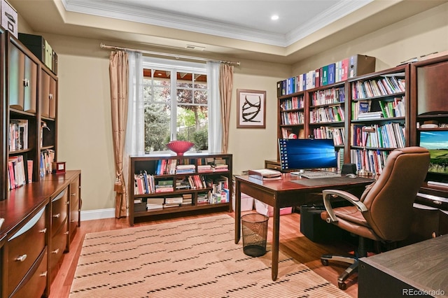 home office featuring light wood-type flooring, ornamental molding, and a raised ceiling