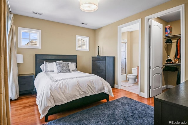 bedroom with a walk in closet, visible vents, baseboards, and wood finished floors