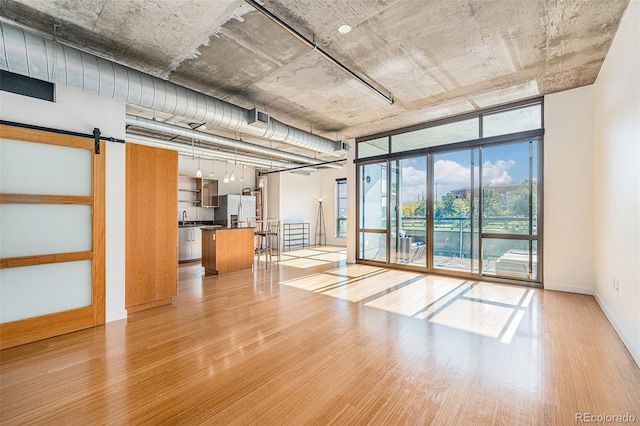 interior space with a barn door, sink, light hardwood / wood-style floors, and stainless steel refrigerator with ice dispenser