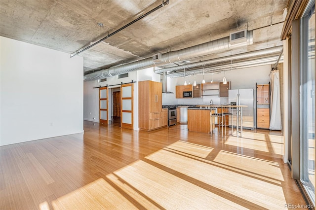 kitchen with a center island, stainless steel appliances, a barn door, hanging light fixtures, and light hardwood / wood-style flooring