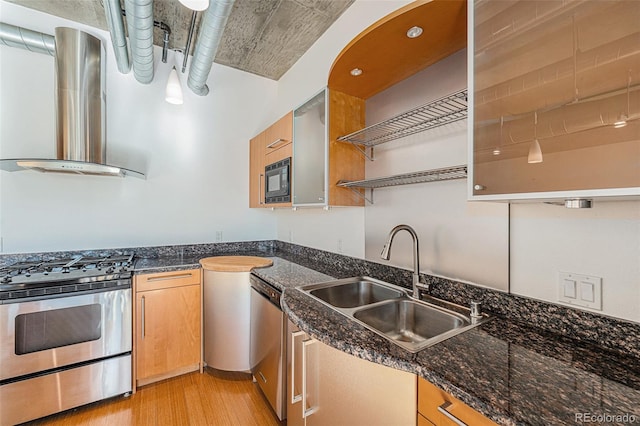 kitchen with sink, light hardwood / wood-style flooring, wall chimney range hood, appliances with stainless steel finishes, and dark stone counters