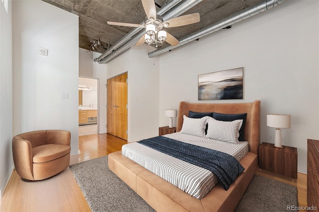 bedroom featuring ceiling fan, light wood-type flooring, connected bathroom, and a high ceiling