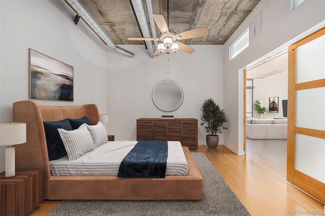 bedroom with light wood-style floors, ceiling fan, a towering ceiling, baseboards, and visible vents