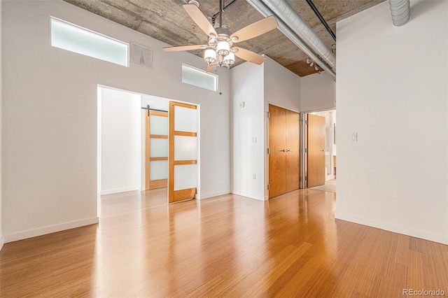 empty room with a barn door, light wood-style floors, a towering ceiling, and ceiling fan