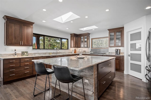 8453 S Scenic Dr, Morrison, CO 80465 - kitchen featuring a skylight, a center island, a breakfast bar, dark wood-type flooring, and glass insert cabinets