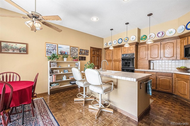 9873 Greensview Cir, Lone Tree, CO 80124 - kitchen with a ceiling fan, tile countertops, brown cabinets, an island with sink, and a high ceiling
