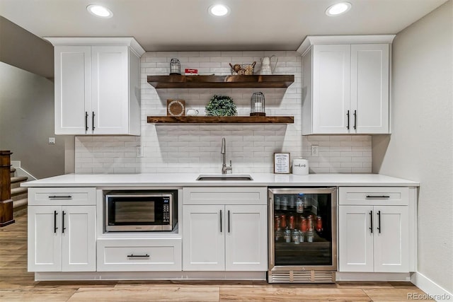 bar featuring sink, wine cooler, stainless steel microwave, tasteful backsplash, and white cabinets