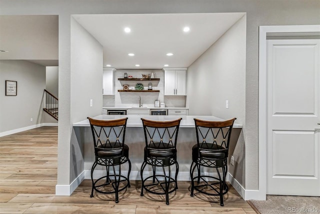 bar with sink, white cabinetry, tasteful backsplash, beverage cooler, and light wood-type flooring