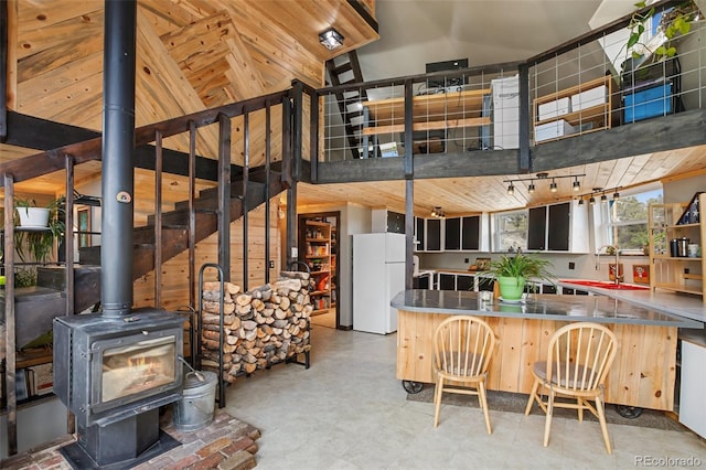 kitchen with freestanding refrigerator, a wood stove, a peninsula, vaulted ceiling, and a sink