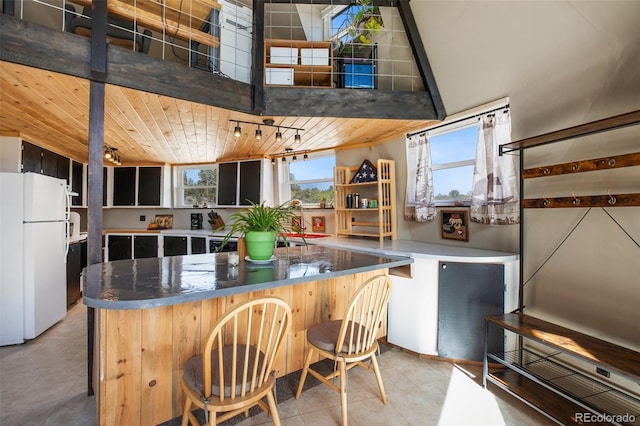 kitchen featuring wooden ceiling, a breakfast bar, a center island, freestanding refrigerator, and tile patterned flooring