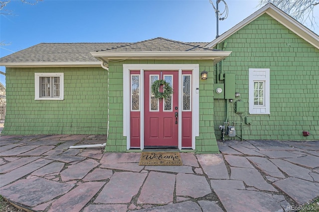 property entrance with a patio area and a shingled roof