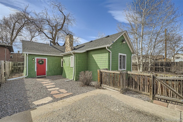 exterior space with a shingled roof, a chimney, and fence