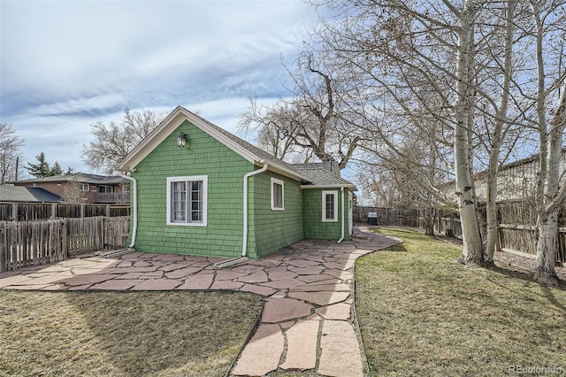 back of house featuring a shingled roof, a lawn, a fenced backyard, and a patio area