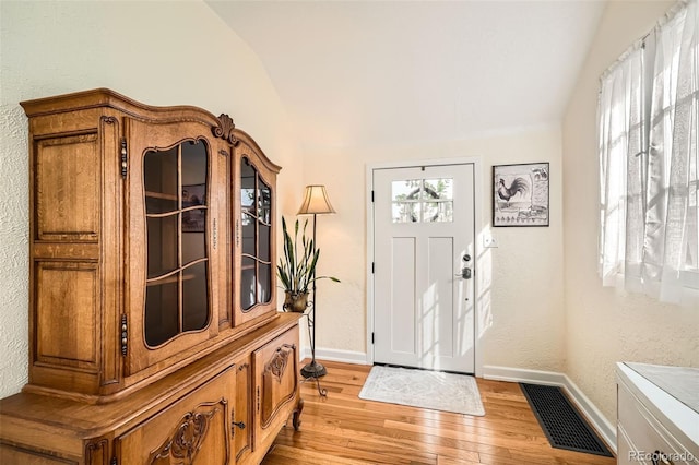 foyer with visible vents, baseboards, light wood finished floors, lofted ceiling, and a textured wall