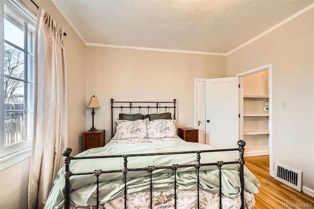 bedroom with light wood finished floors, visible vents, a textured ceiling, and crown molding