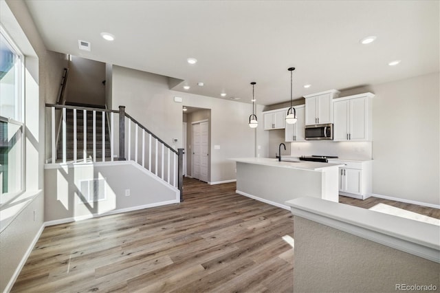 kitchen with light wood-type flooring, a kitchen island with sink, sink, pendant lighting, and white cabinetry