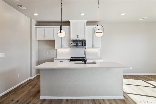 kitchen with sink, tasteful backsplash, pendant lighting, wood-type flooring, and a kitchen island with sink