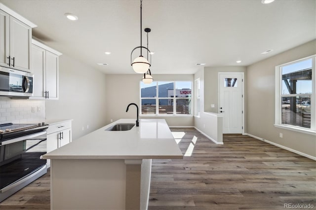 kitchen with a kitchen island with sink, white cabinets, hanging light fixtures, sink, and appliances with stainless steel finishes