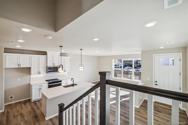 kitchen with stainless steel appliances, sink, decorative light fixtures, white cabinets, and an island with sink