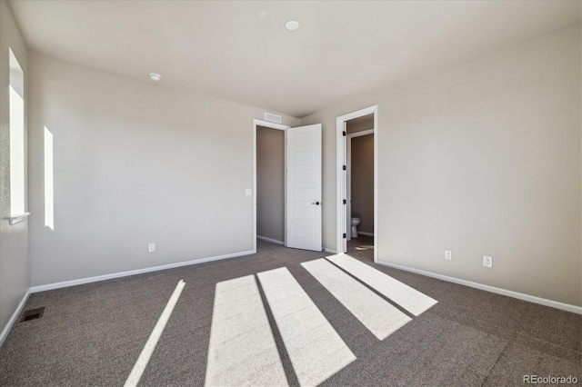 unfurnished bedroom with ensuite bathroom and dark colored carpet