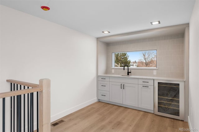 bar featuring decorative backsplash, light wood-type flooring, beverage cooler, sink, and white cabinets