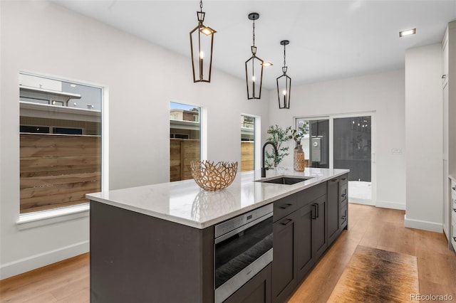 kitchen featuring light wood-type flooring, light stone counters, sink, pendant lighting, and a center island with sink