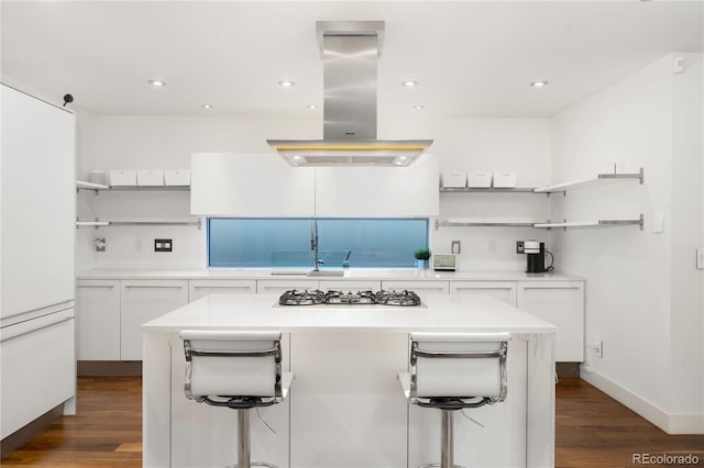 kitchen with island exhaust hood, built in fridge, white cabinets, and a kitchen bar