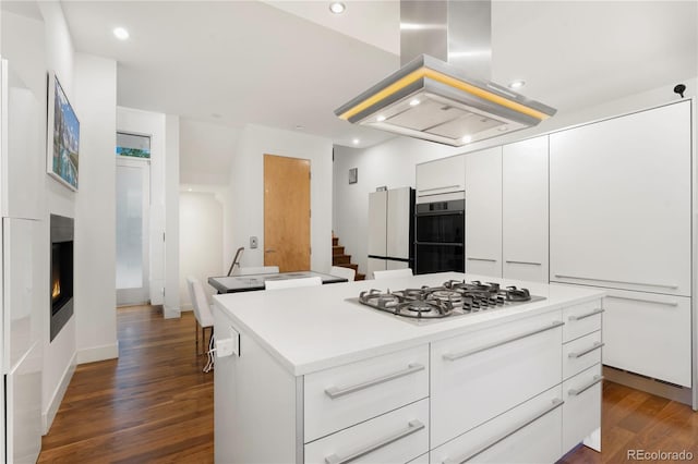 kitchen with white fridge, white cabinetry, island range hood, stainless steel gas cooktop, and a kitchen island