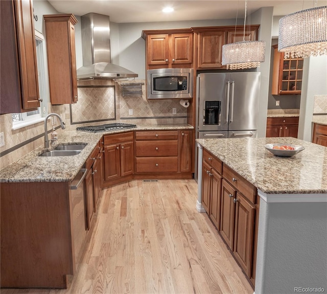 kitchen with sink, appliances with stainless steel finishes, a kitchen island, pendant lighting, and wall chimney range hood