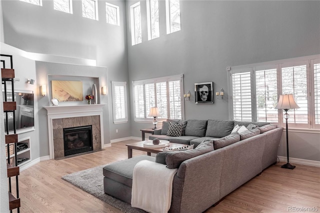 living room featuring a tiled fireplace, a high ceiling, and light wood-type flooring