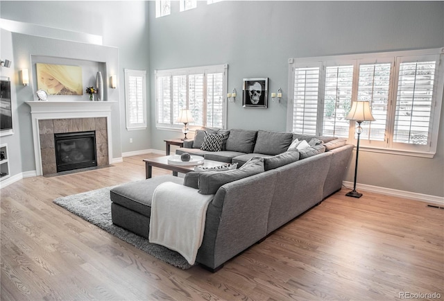 living room with a tile fireplace, light hardwood / wood-style floors, plenty of natural light, and a high ceiling