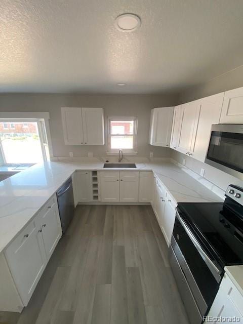 521 10th St, Fort Lupton, CO 80621 - kitchen featuring appliances with stainless steel finishes, a sink, a textured ceiling, white cabinetry, and wood finished floors