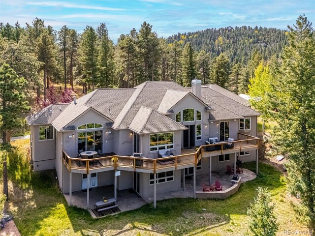 rear view of house with a wooded view, a chimney, a deck, a yard, and a patio area