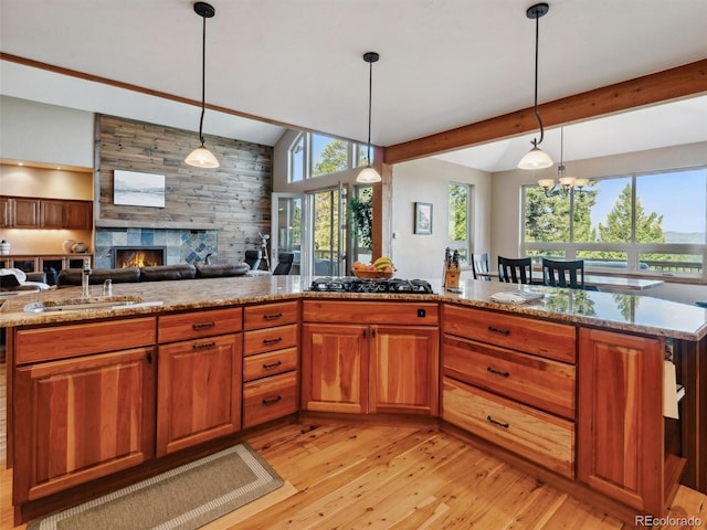 kitchen with a sink, lofted ceiling with beams, black gas cooktop, a fireplace, and light wood finished floors