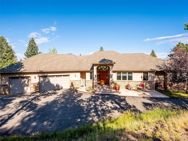 view of front of property featuring stucco siding, stone siding, a garage, and driveway